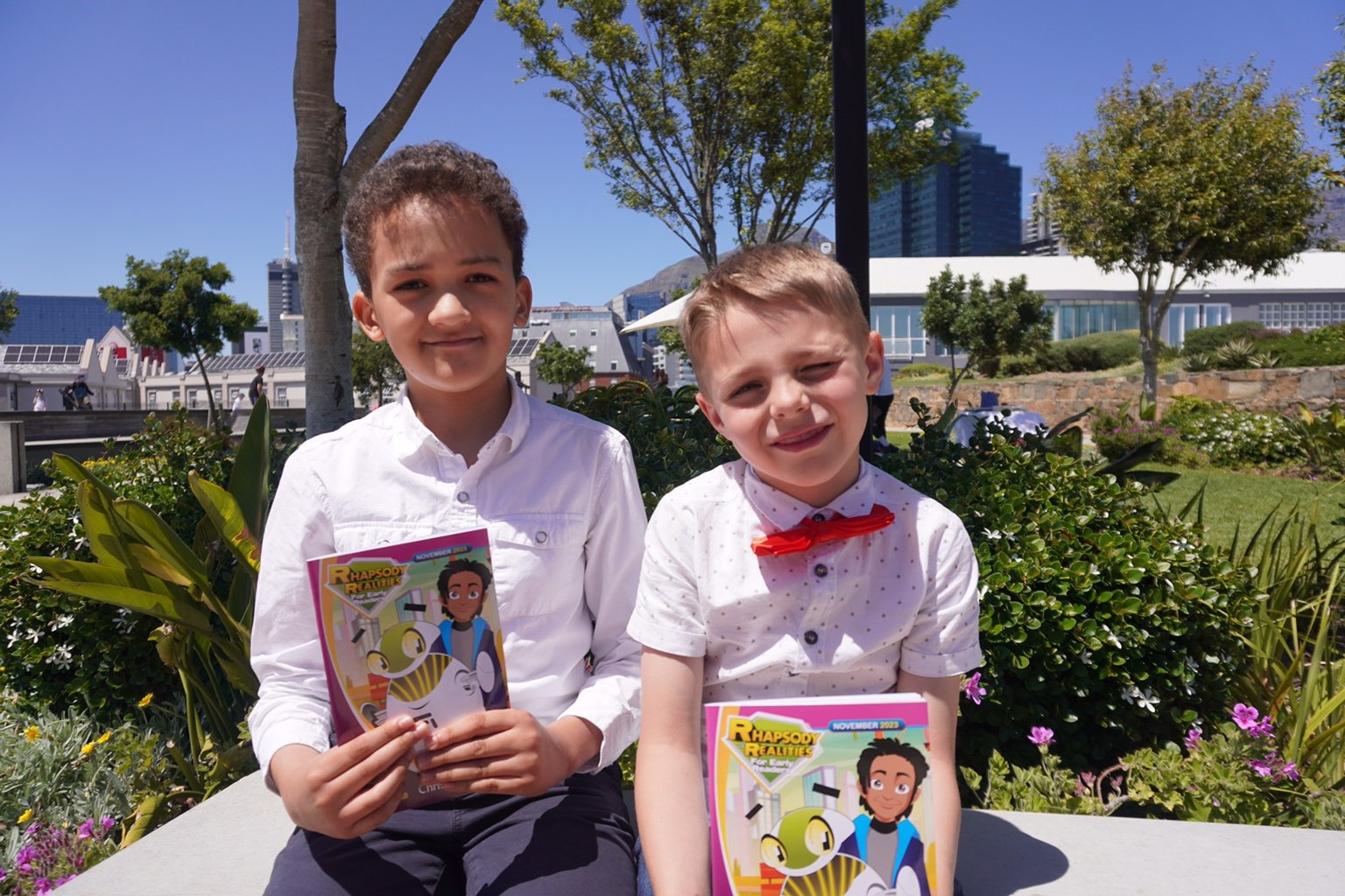 Two boys holding copies while seated in a bright garden space.